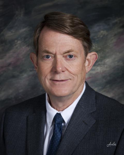 A man in a dark grey tweed suit with a blue tie