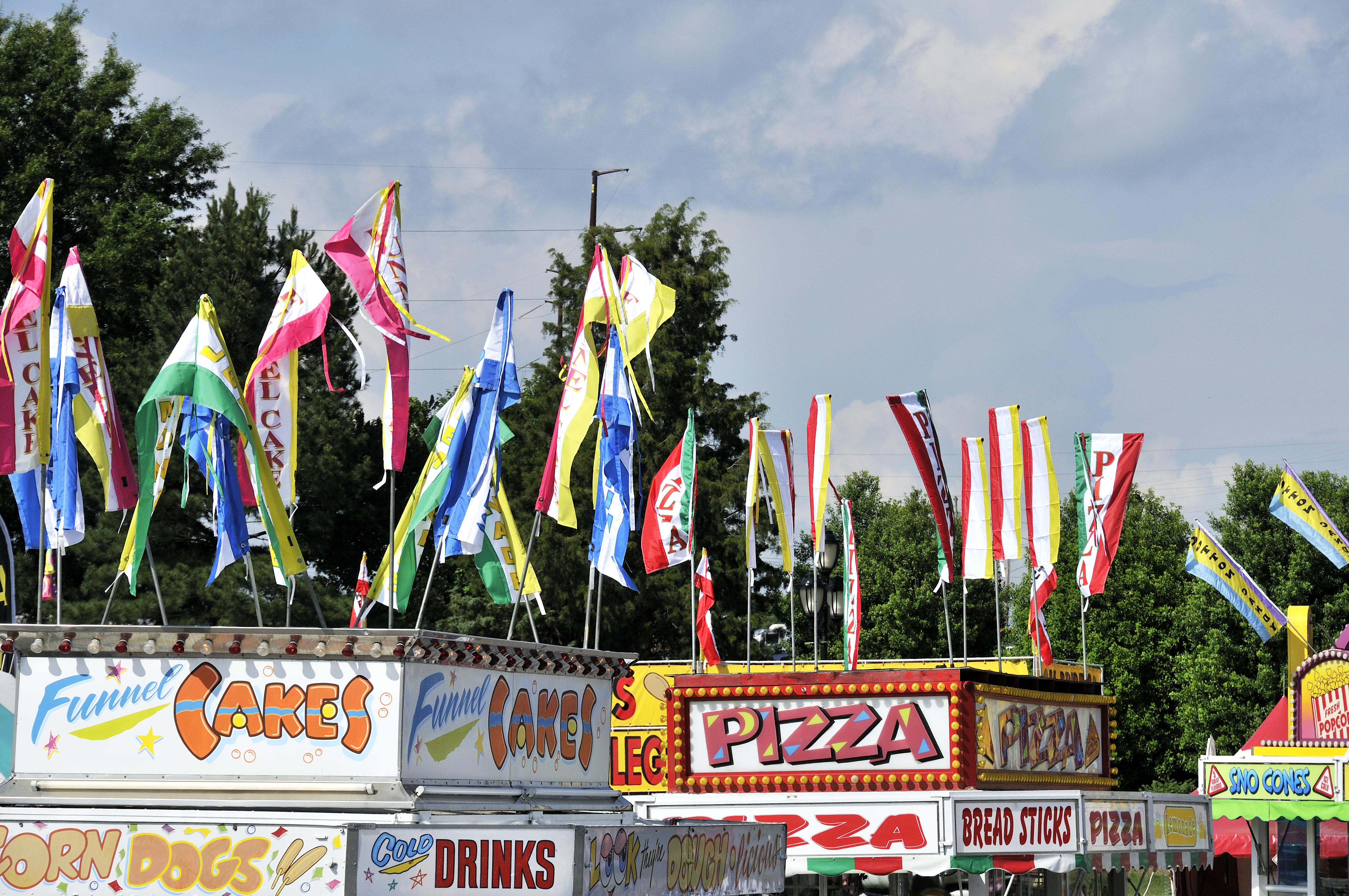 Multiple carnival food stands with colorful flags and signs 