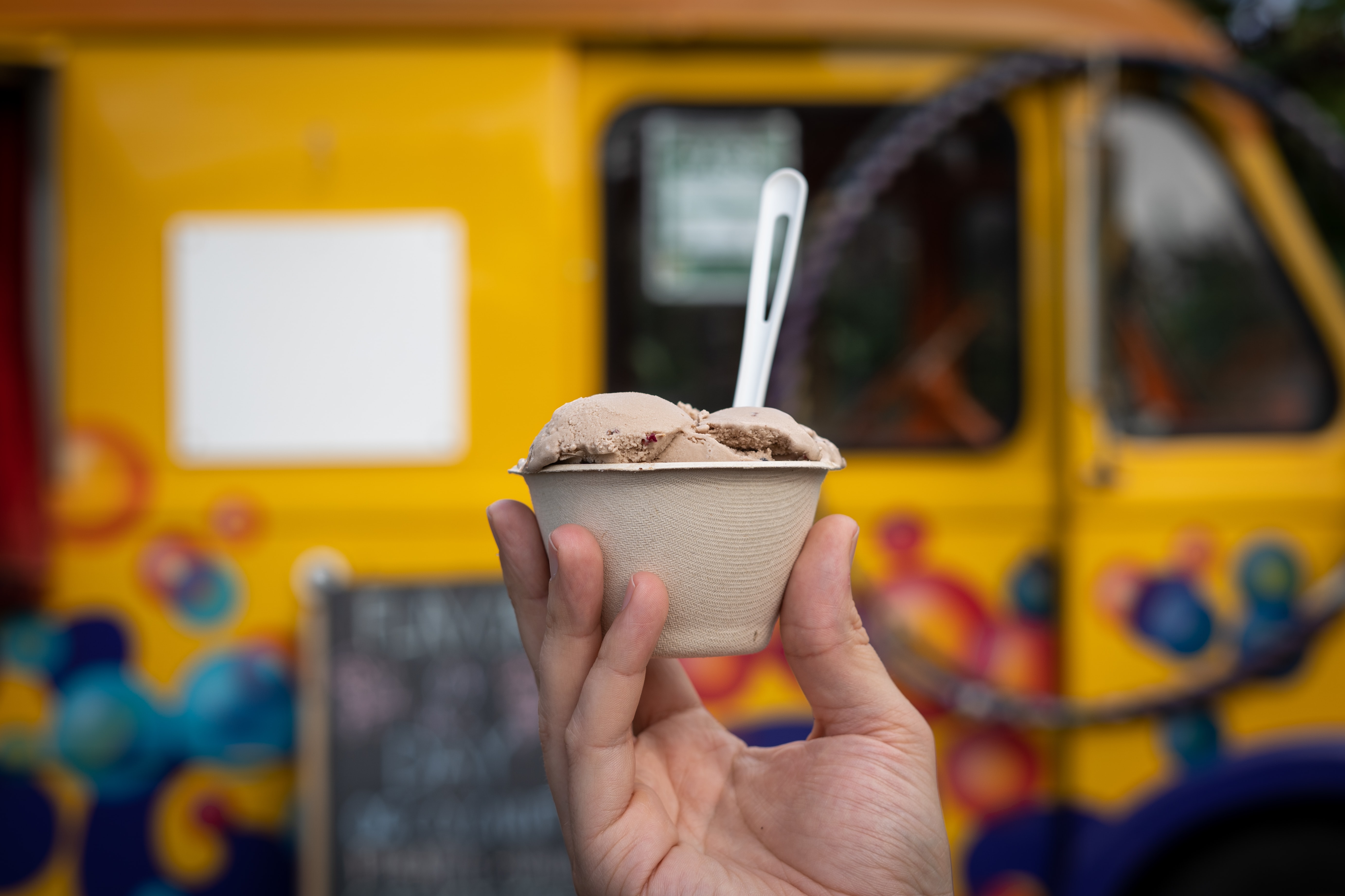 A hand holding a cup of chocolate ice cream in front of an ice cream truck