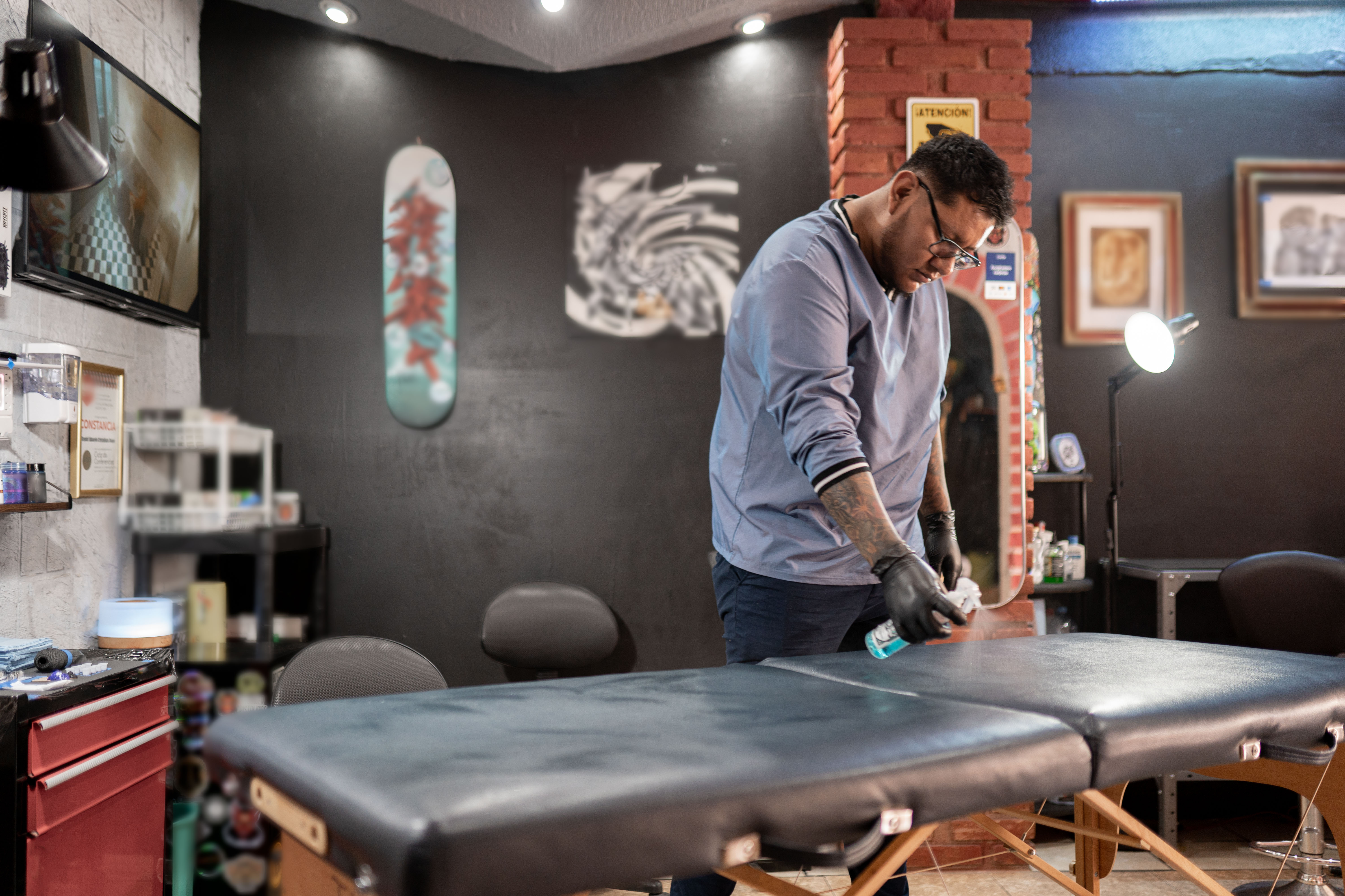 A tattoo artist cleaning the studio stretcher with a spray