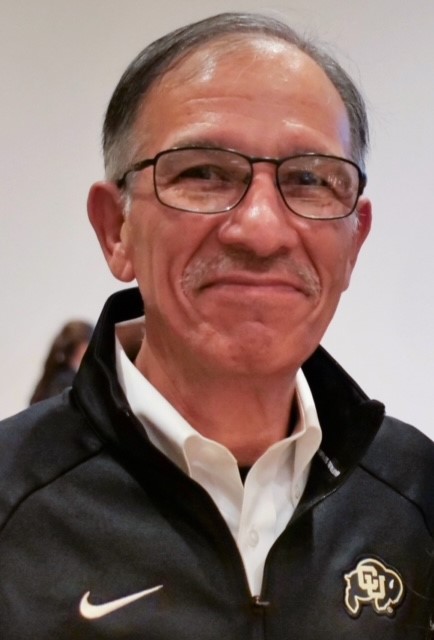 A man with glasses wearing a white polo shirt and black athletic jacket